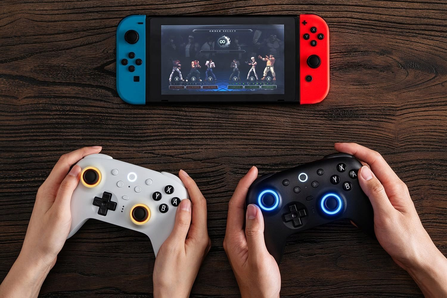 Nintendo Switch z grą walki na ekranie, dwa kontrolery. Jeden biały, drugi czarny. Ręce trzymające je, na drewnianym stole.