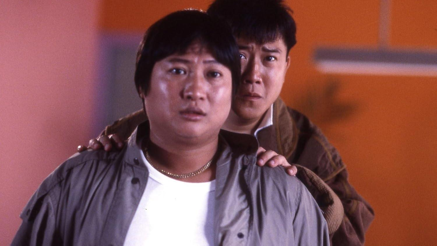 Zwei asiatische Männer. Einer vorn, besorgt, trägt eine Jacke und ein weißes Hemd. Der andere Mann hinter ihm.