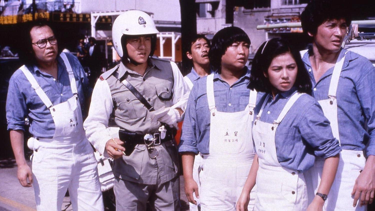 Gruppe von Menschen in Uniform, einige tragen Overalls. Ein Polizist mit weißem Helm steht im Zentrum und schaut zu.
