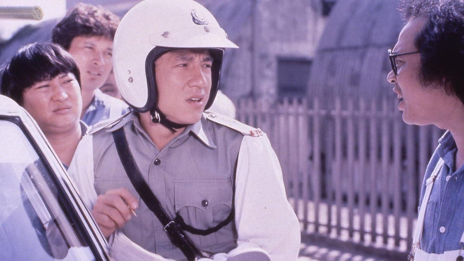 Ein Mann mit weißem Helm und Uniform blickt besorgt, umgeben von anderen, in der Nähe eines Autos. Ein anderer Mann trägt eine Brille.