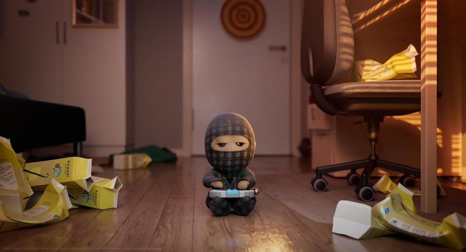 Eine Ninja-Puppe sitzt auf einem Holzboden und hält eine Spielkonsole. Milchkartons und ein Stuhl sind im Hintergrund.