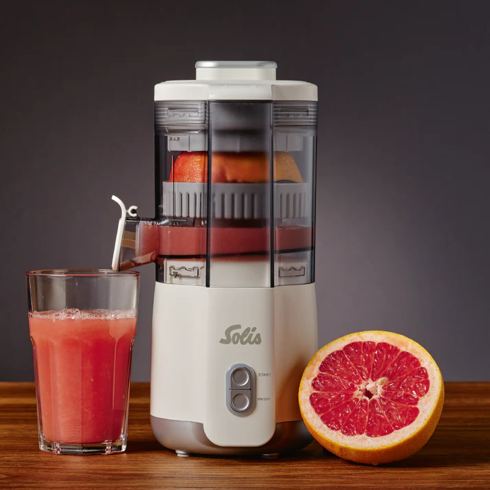 Una centrifuga estrae il succo da un pompelmo. Un bicchiere di succo e un pompelmo a metà su un tavolo di legno.
