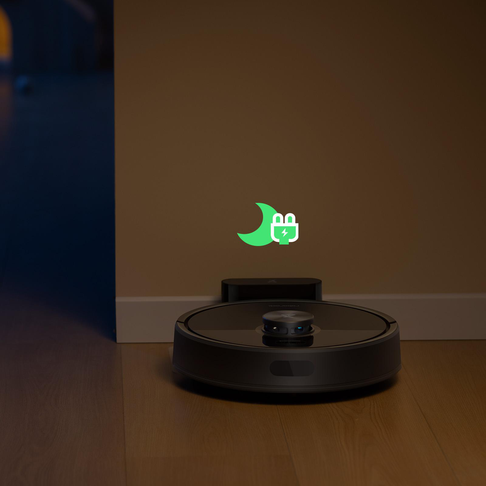 Ein schwarzer Roboter-Staubsauger auf einem Holzboden in der Nähe einer Wand. Ein Ladesymbol wird angezeigt.