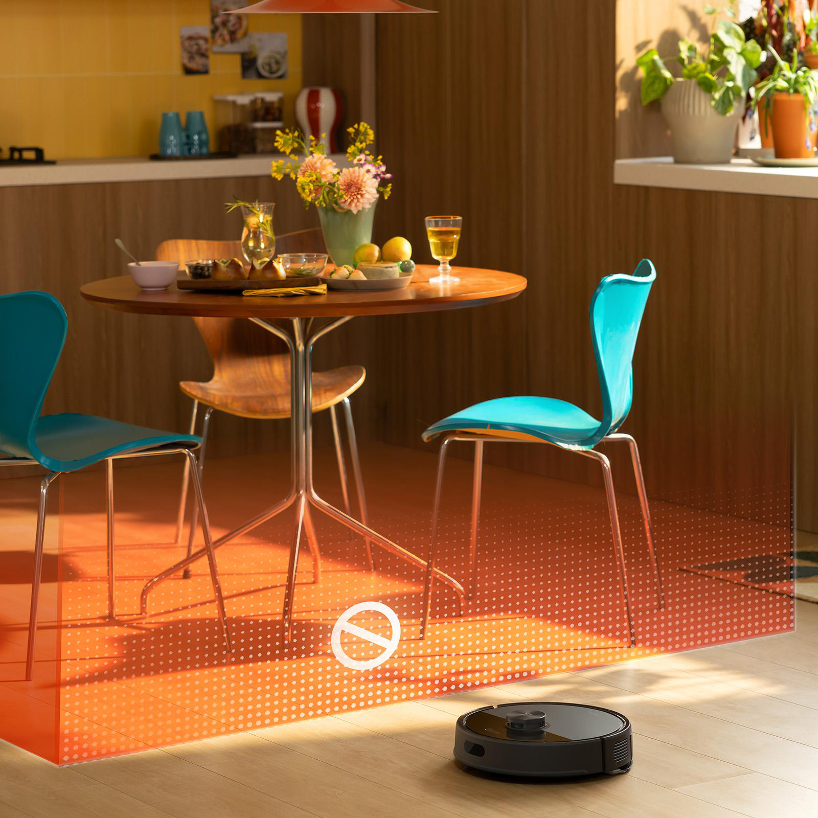 Eine Esszene mit einem runden Tisch für eine Mahlzeit, blauen Stühlen und einem Roboter-Staubsauger auf dem Boden.