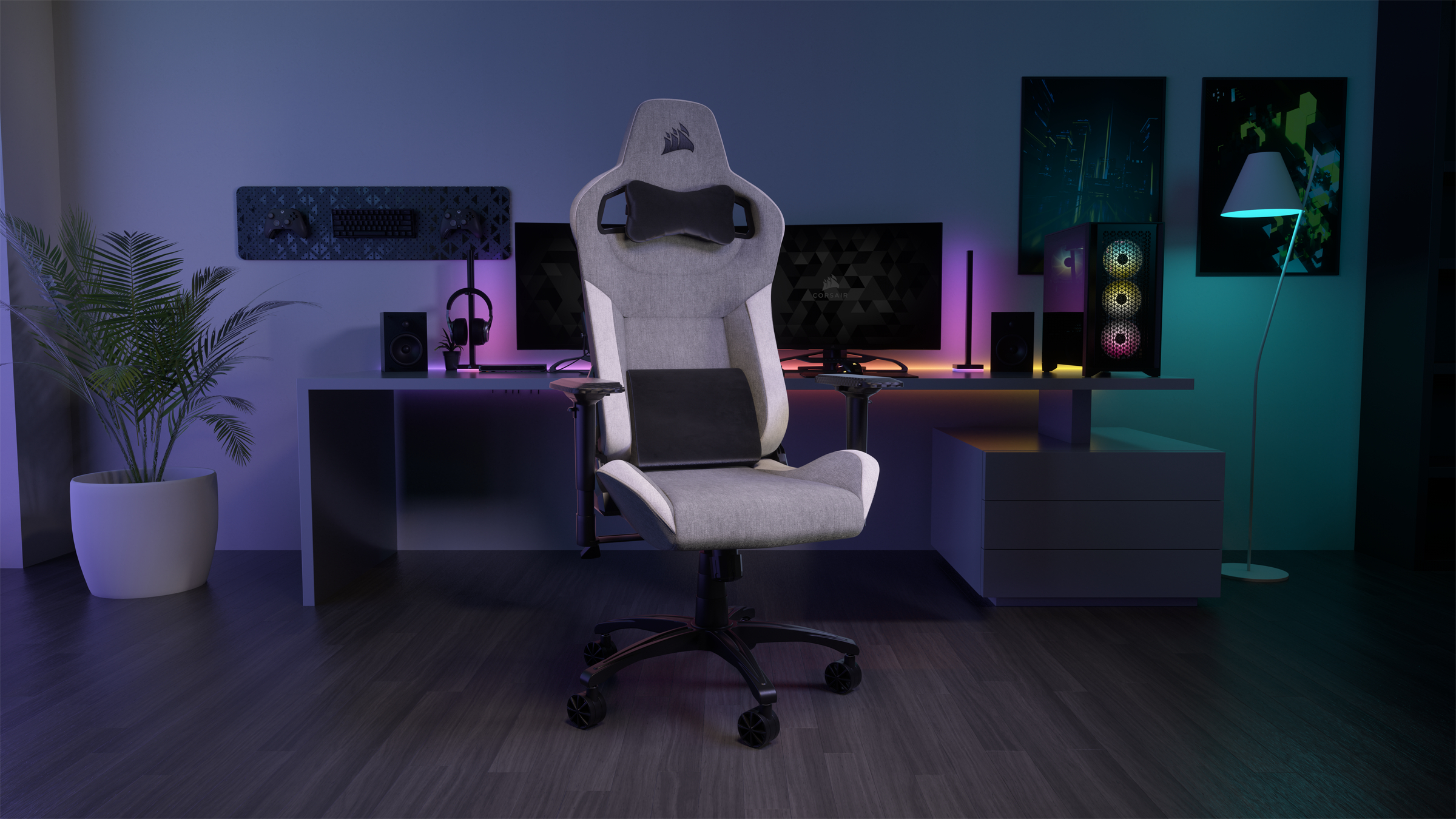 Gaming-Stuhl in einem Raum mit Schreibtisch, Computer und Zubehör. Eine Pflanze, Kunst und eine Lampe sind ebenfalls vorhanden.