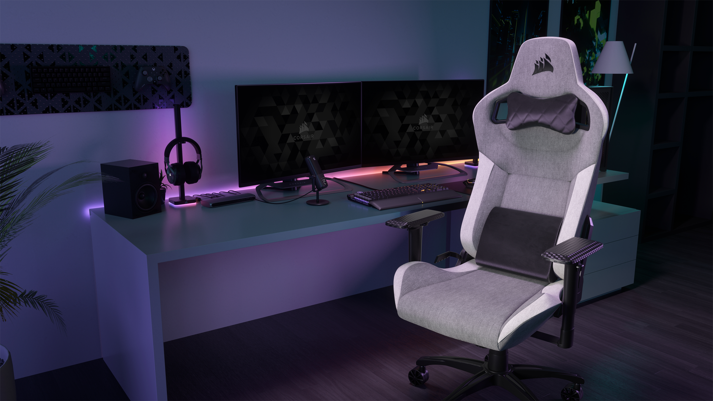 Gaming-Setup mit grauem Stuhl, zwei Monitoren, Tastatur und Headset. Lila und weiße Beleuchtung schaffen eine moderne Ästhetik.