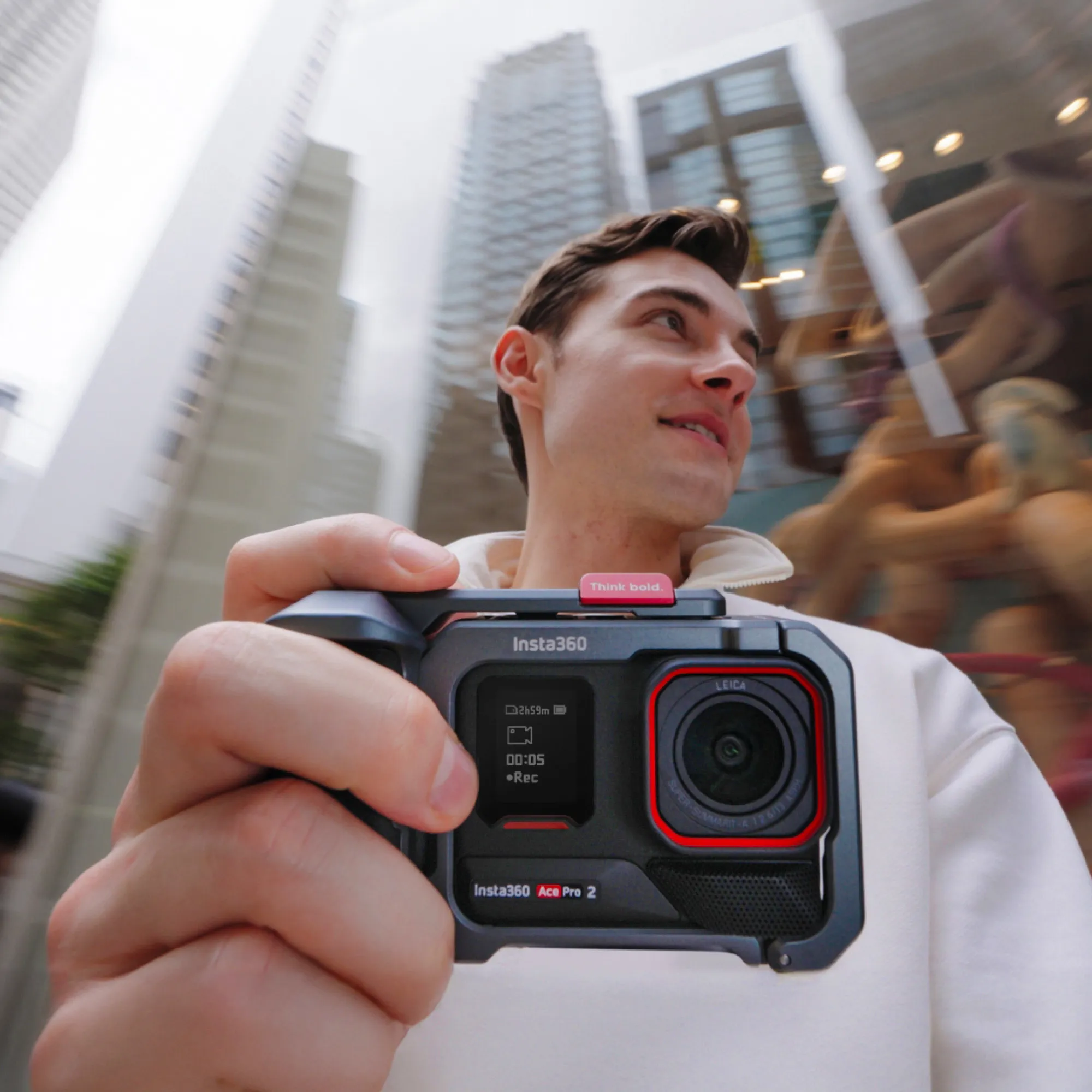 Ein Mann hält eine Insta360 Ace Pro 2 Kamera. Gebäude sind verschwommen im Hintergrund. Der Mann lächelt.