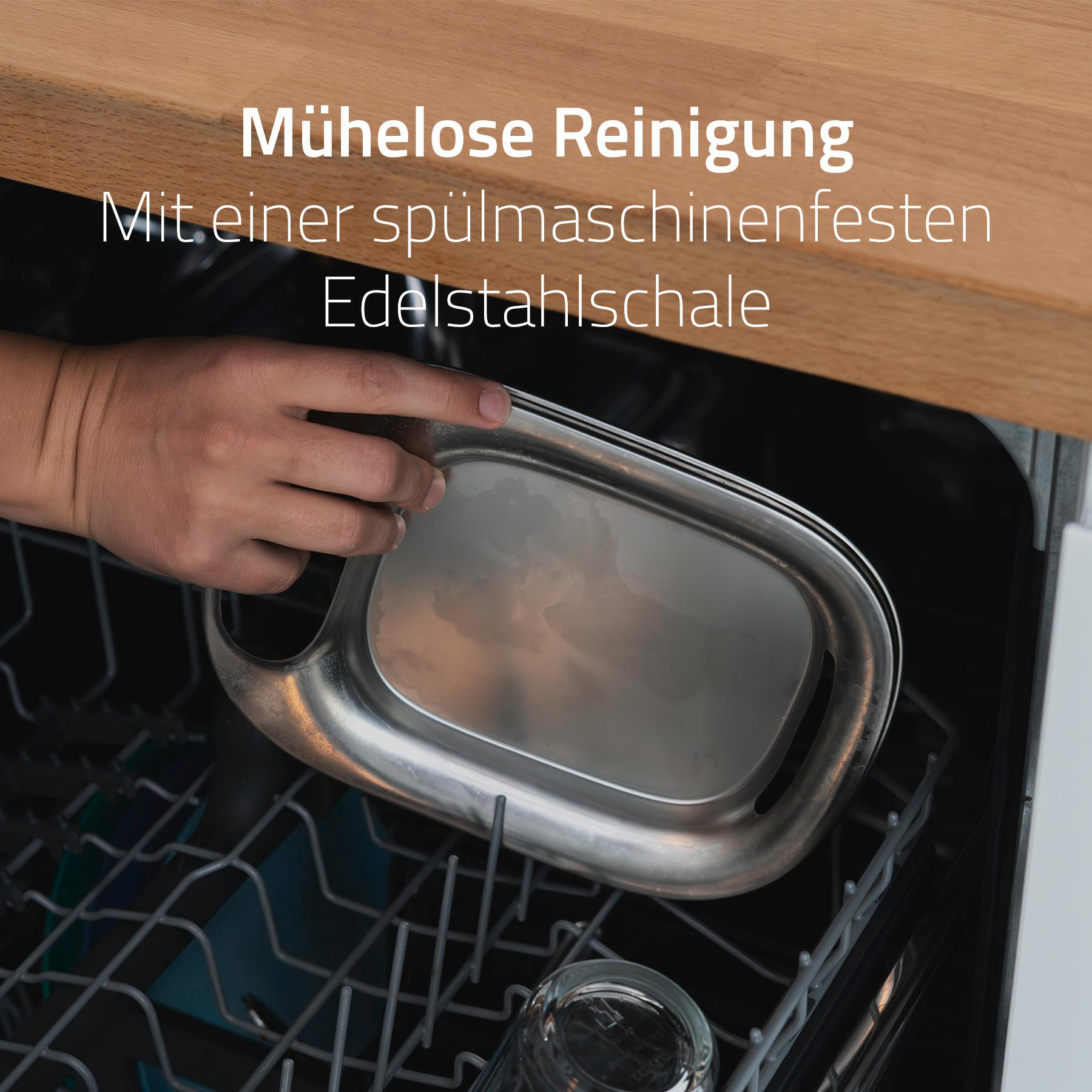 Eine Hand legt ein Edelstahl-Tablett in einen Geschirrspüler. Das Tablett ist rechteckig mit abgerundeten Kanten.
