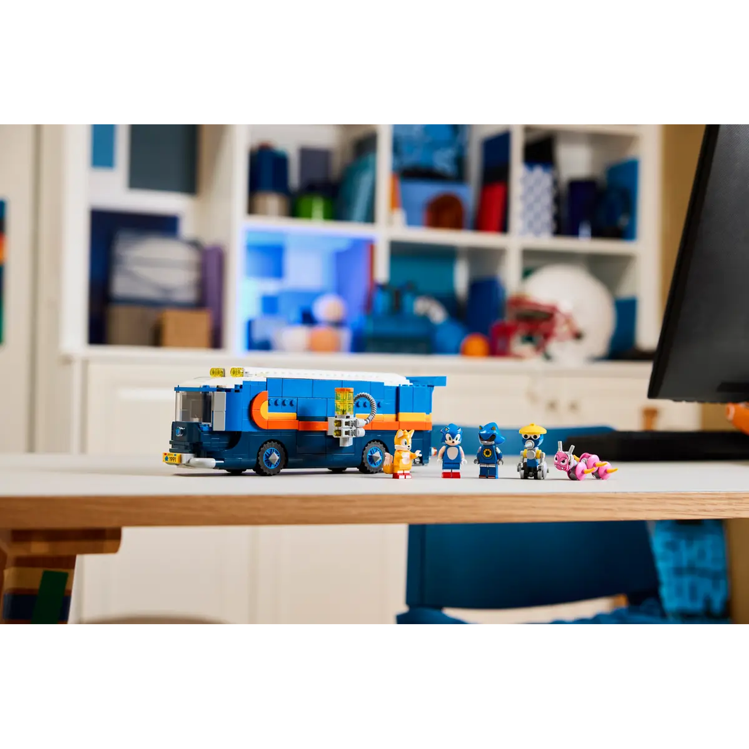 Een blauw-oranje Lego-bus met Sonic-personages. De bus staat op een tafel met een witte plank en een zwarte computer op de achtergrond.
