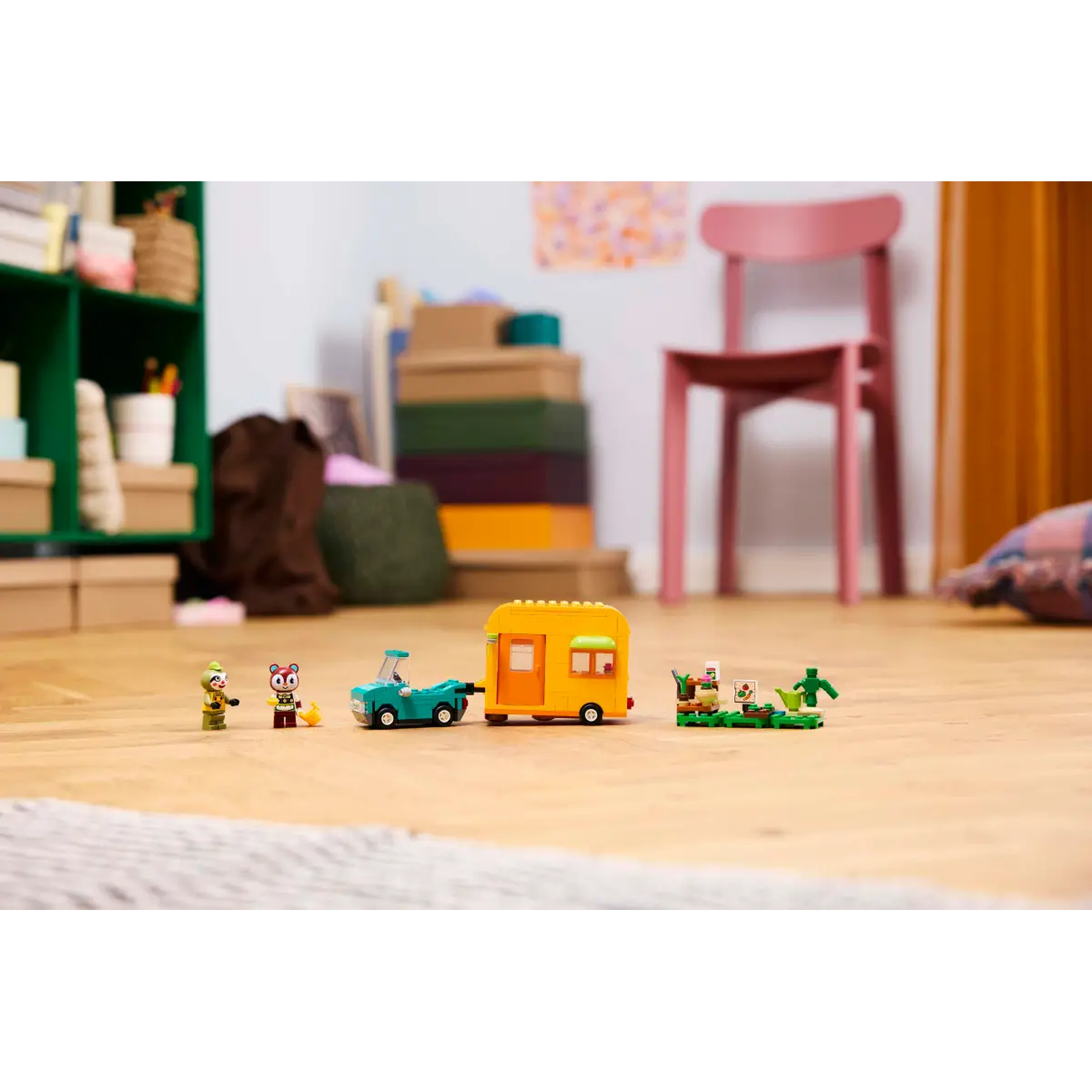 Een Lego-scène met kleine figuren, een blauwgroene auto die een gele caravan trekt en een kleine tuin.