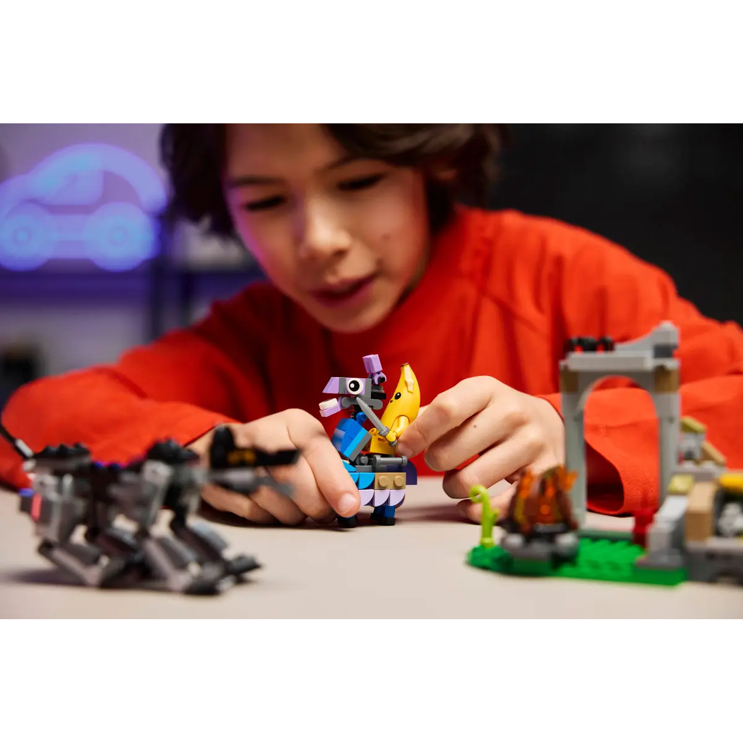 A child in red plays with colorful Lego. A Lego dragon, a banana, and a small structure are visible.