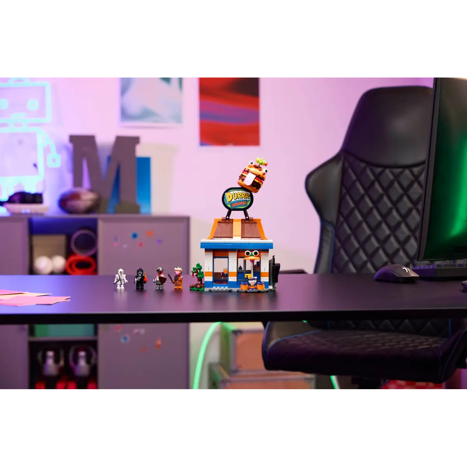 Lego set: Burger shop met minifiguren op een zwart bureau. Achtergrond heeft een stoel, computer en wanddecoraties.