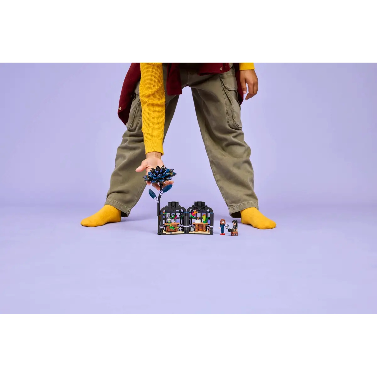 Une personne tient une fleur bleue au-dessus d'un jeu Lego de deux bâtiments. L'ensemble contient des mini-figurines et divers objets.