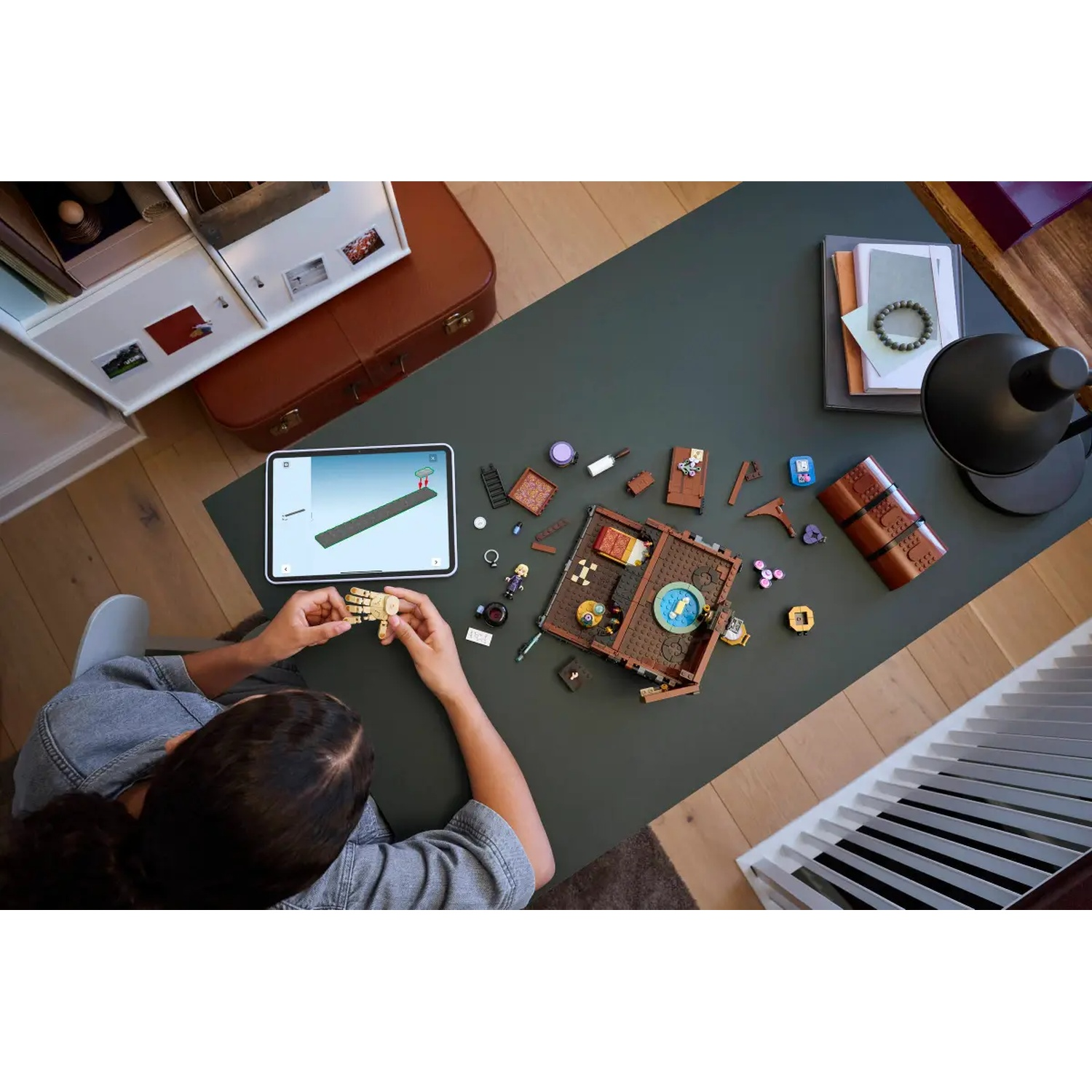 Een persoon bouwt een Lego-set op een groene tafel. Er is een tablet, Lego-onderdelen en andere items.
