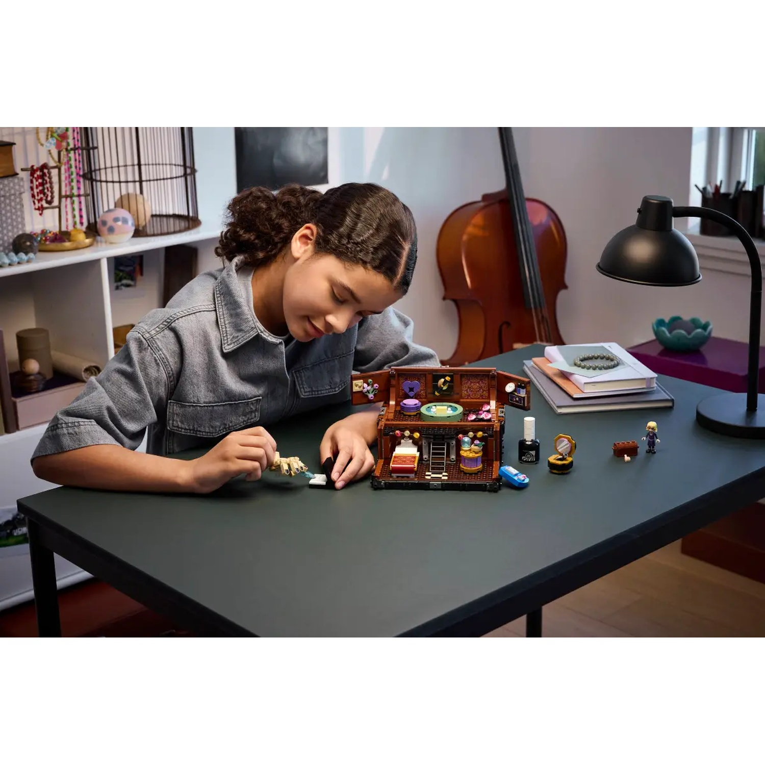 Een meisje speelt met een Lego-set op een donkergroene tafel. Op de achtergrond staat een cello, een lamp en andere voorwerpen zijn zichtbaar.