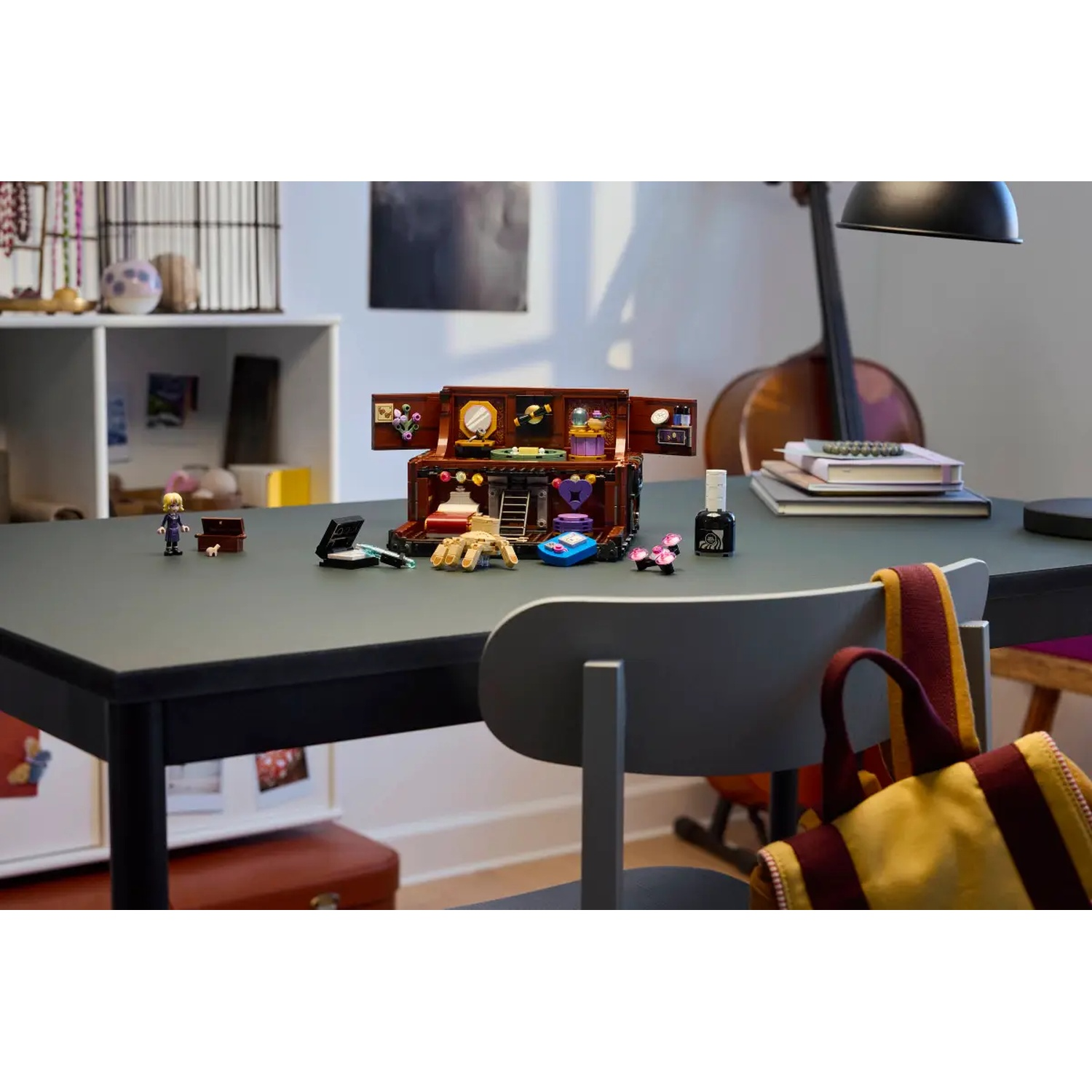 Een Lego-set met een koffer, figuren en accessoires op een tafel. Een cello, lamp en boeken op de achtergrond.