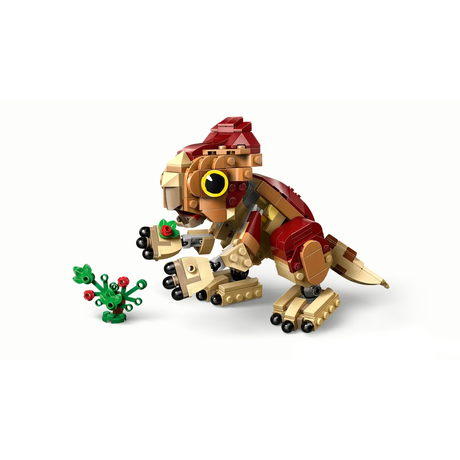 A Lego dinosaur with red and tan blocks. It has a yellow eye. A green plant with red berries is in front of it.