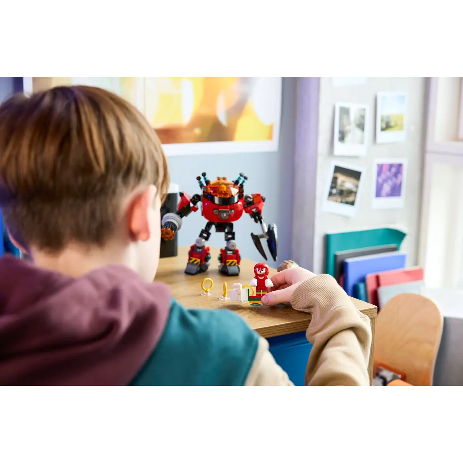 Un enfant joue avec des figurines Lego Sonic. Un robot rouge et des figurines sont sur une table en bois. Une étagère avec des photos est en arrière-plan.