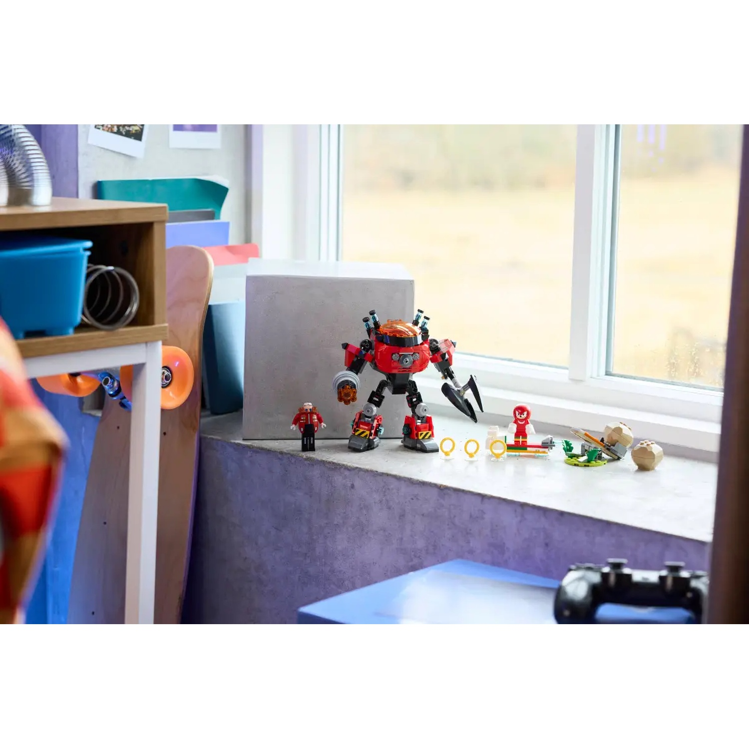 Un robot jouet rouge et noir, de petites figurines, des anneaux et une manette sur un rebord de fenêtre. Un skateboard et des étagères en arrière-plan.