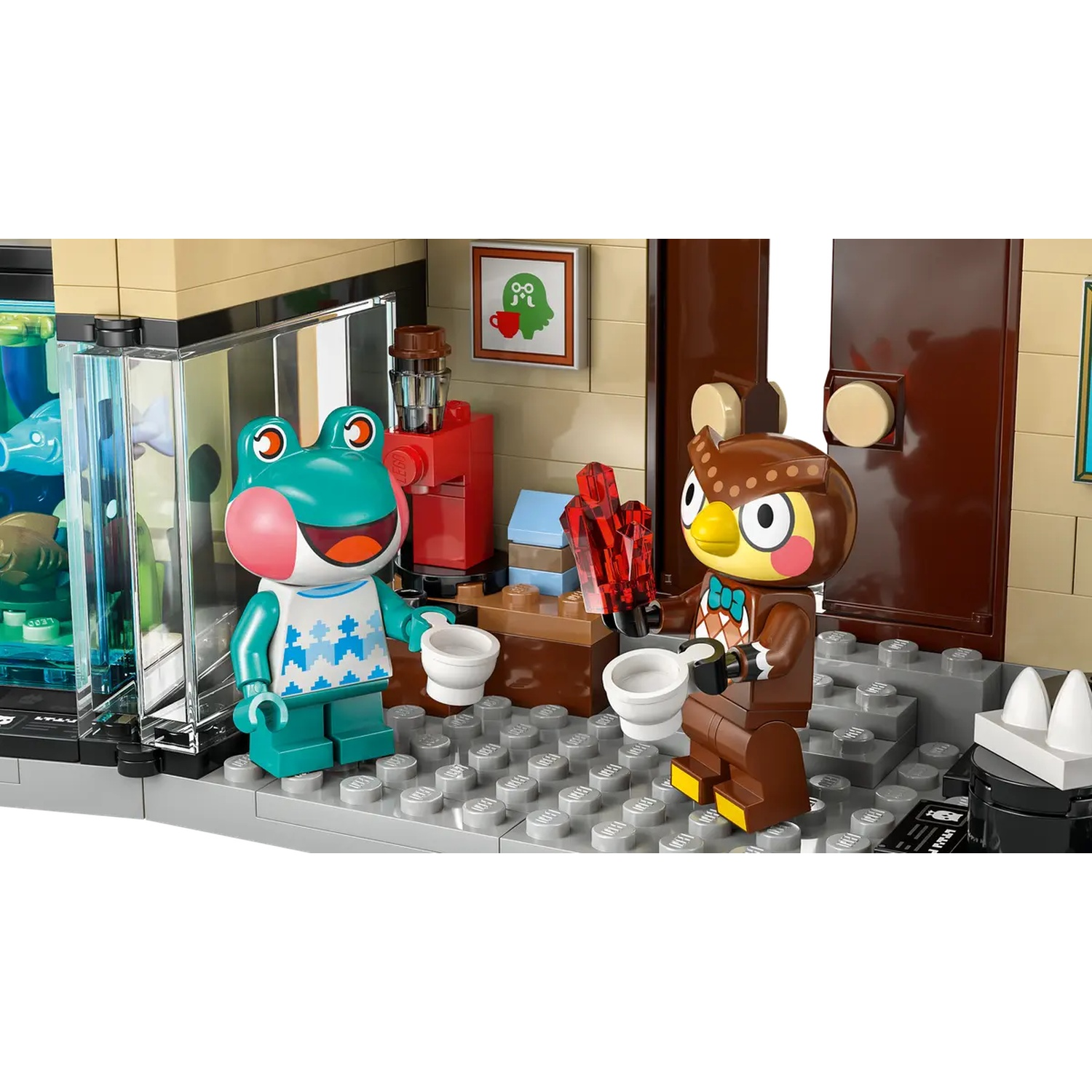 Scène Lego avec des figurines de grenouille et de hibou tenant des tasses. Une machine à café rouge et une image sont accrochées au mur, avec une porte.