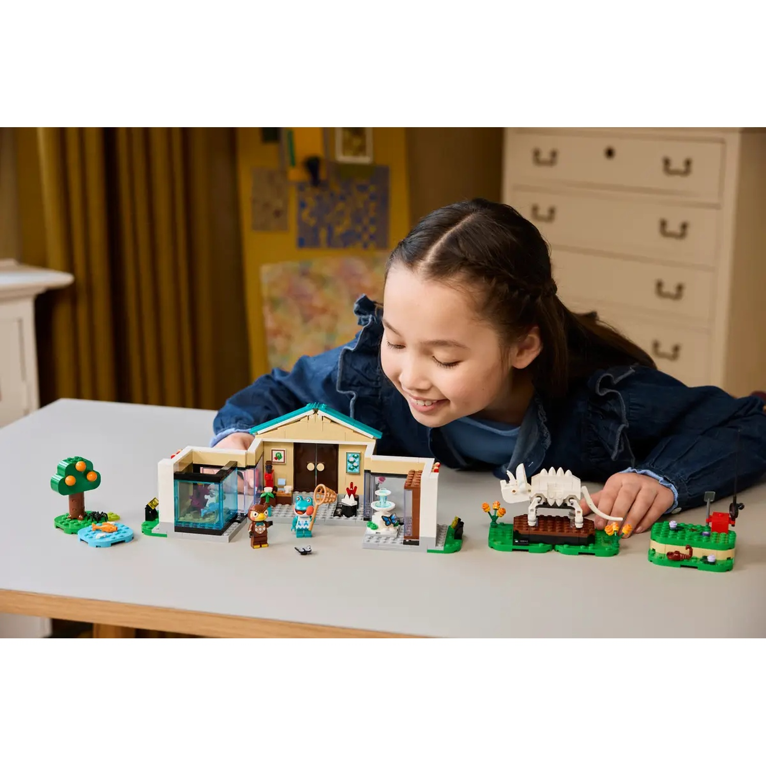 Une fille regarde un jeu Lego. L'ensemble comprend une maison, un arbre, de petites figurines et un squelette de dinosaure.