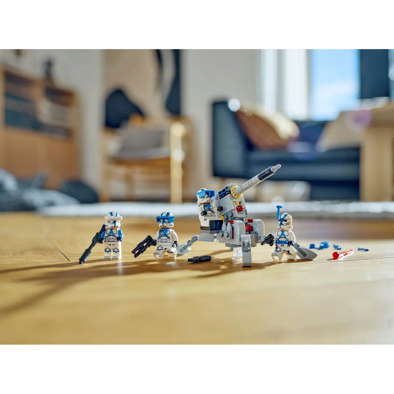 Lego Star Wars set. Clone troopers with blasters and a cannon on a wooden floor. Background shows a blurred room with furniture.