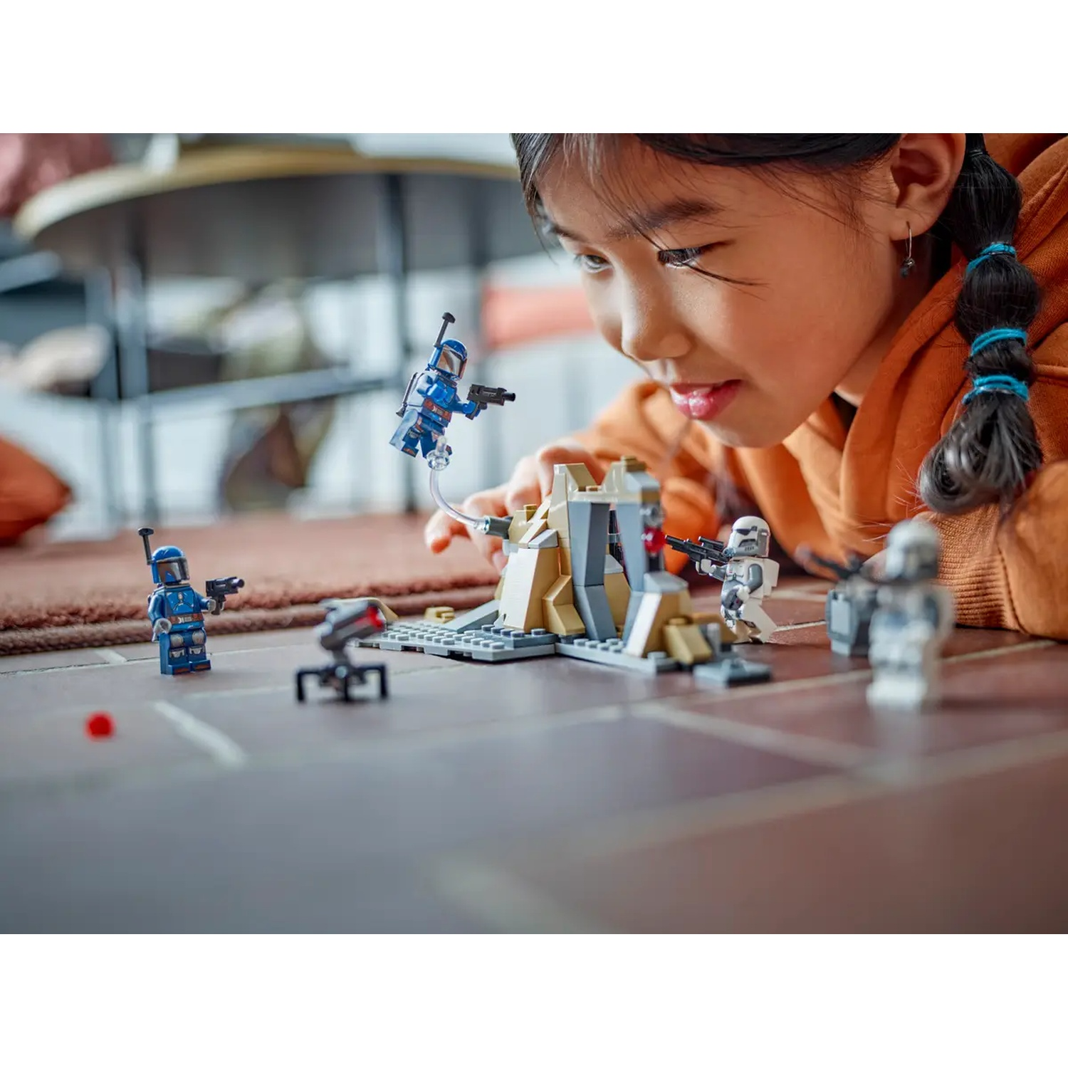 A young girl plays with Star Wars Lego. Blue and white Lego figures are on the floor. A Lego structure is in the center.