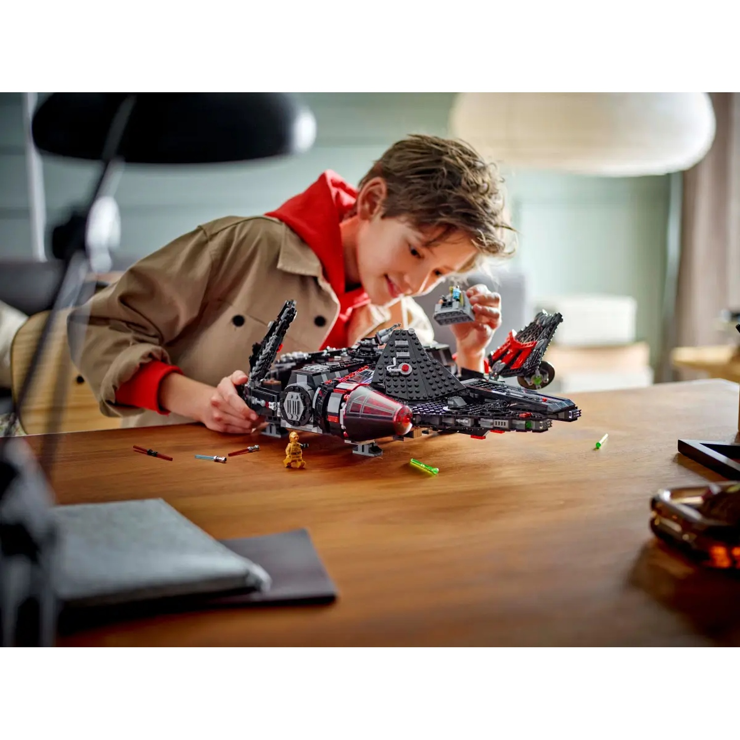 A boy with a Lego spaceship on a table. He is holding a small Lego figure and looking at the spaceship with a smile.