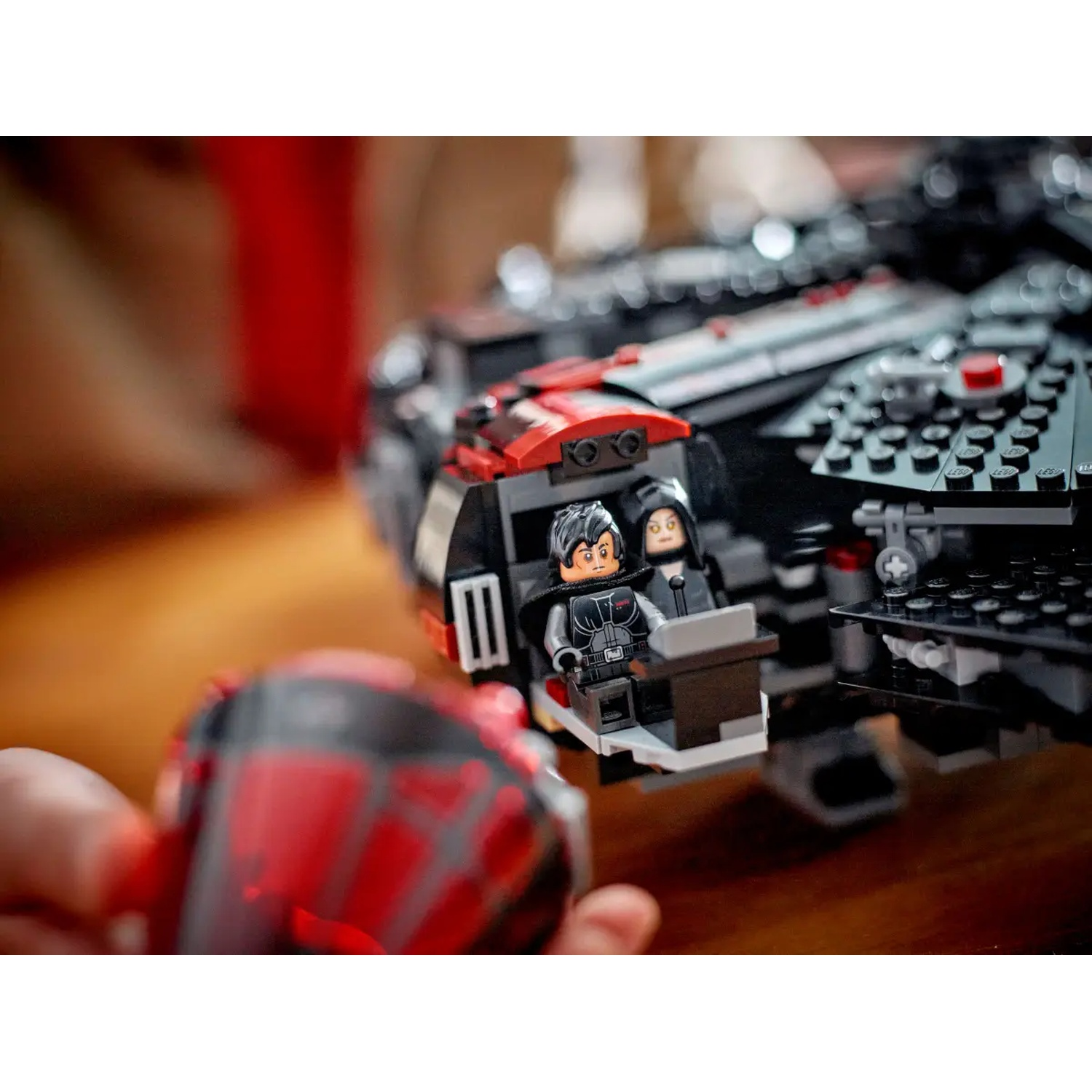 Lego Star Wars set with two minifigures in a cockpit. The ship is black and red. A hand holds a red piece.