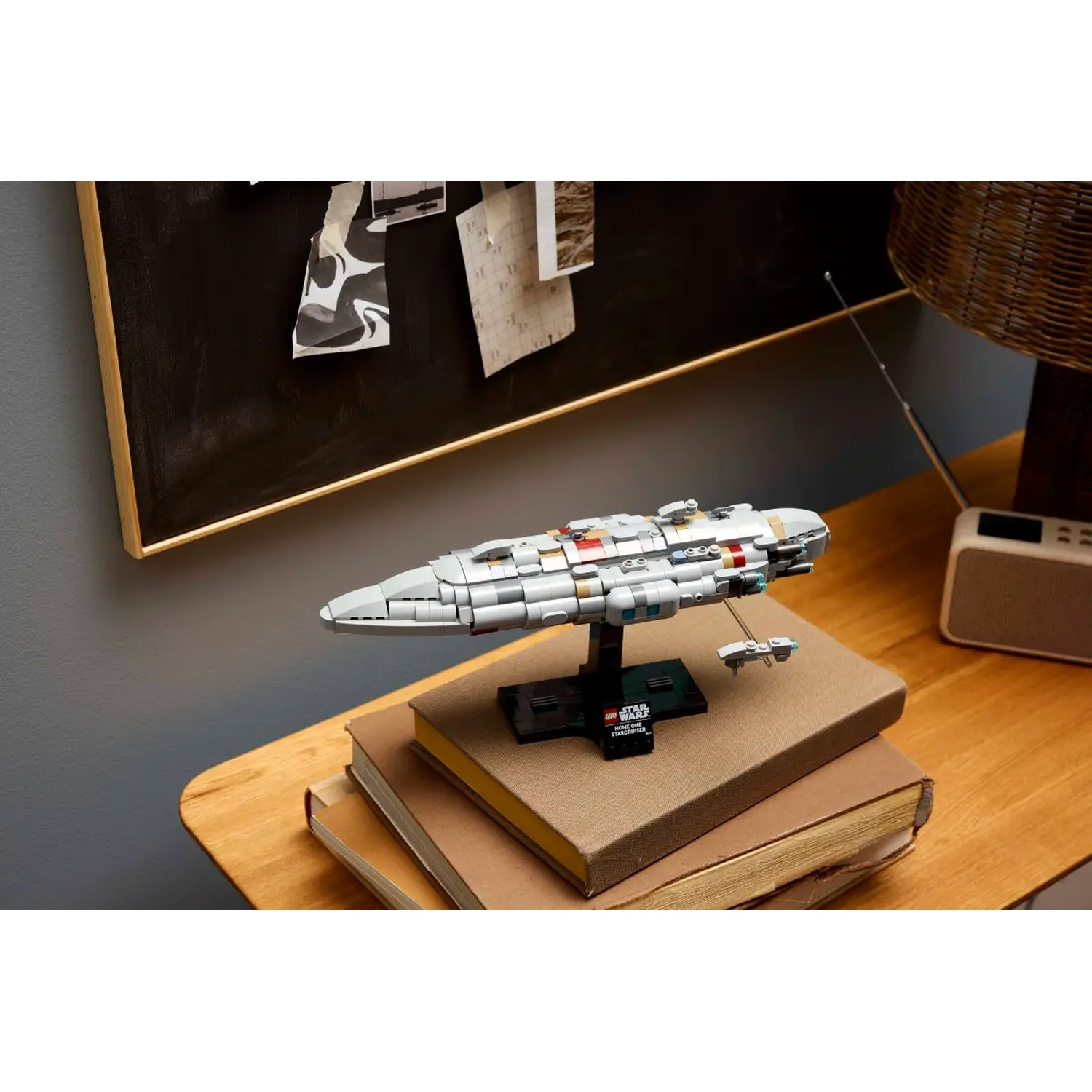 A Star Wars Lego model of a spaceship on a stack of books, on a wooden table. A bulletin board is in the background.