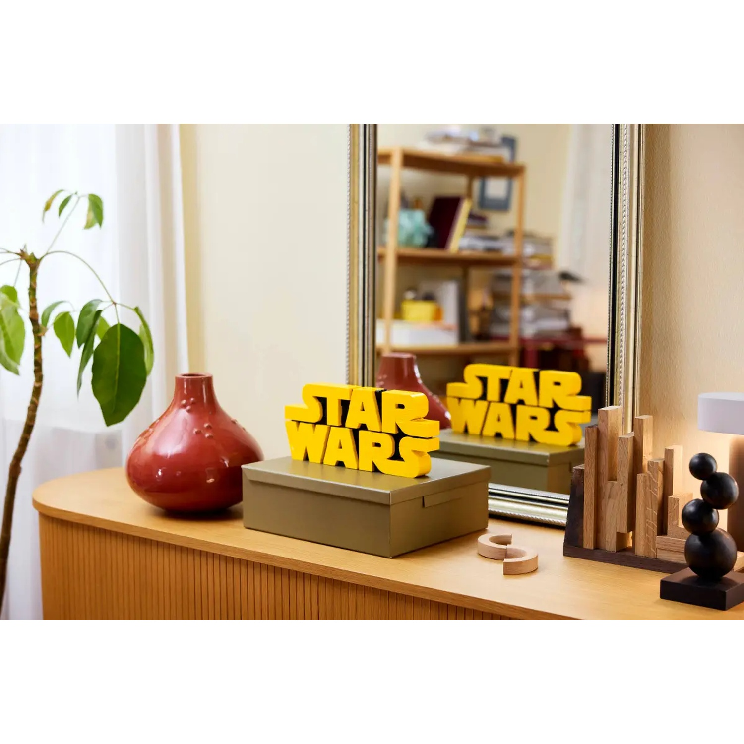 Een houten kast met een rode vaas, een doos met een geel Star Wars-bord en een spiegel die hetzelfde reflecteert.