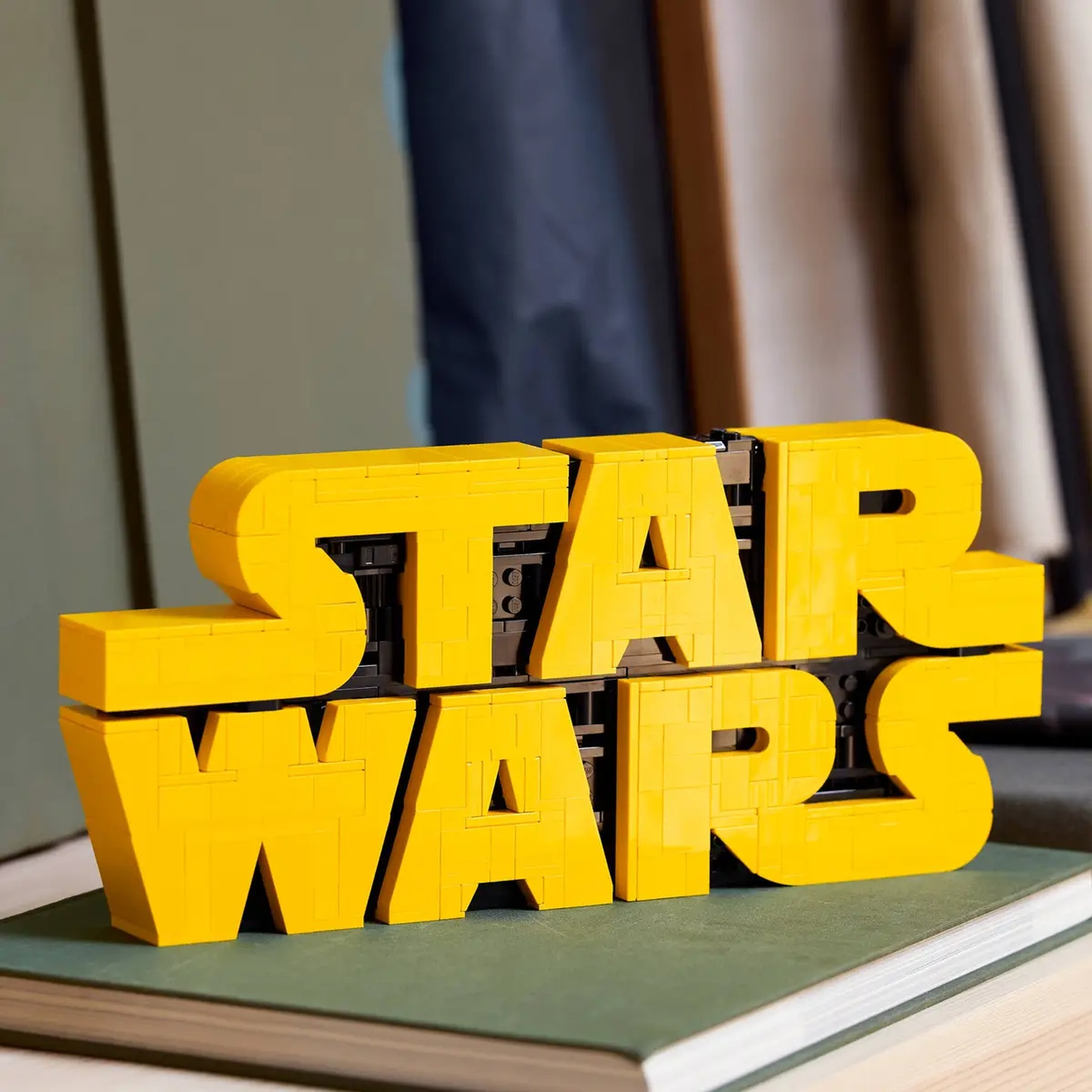 Een Lego "STAR WARS" bord. Gele letters op een boek met groene kaft. Achtergrond: muur en gordijnen.
