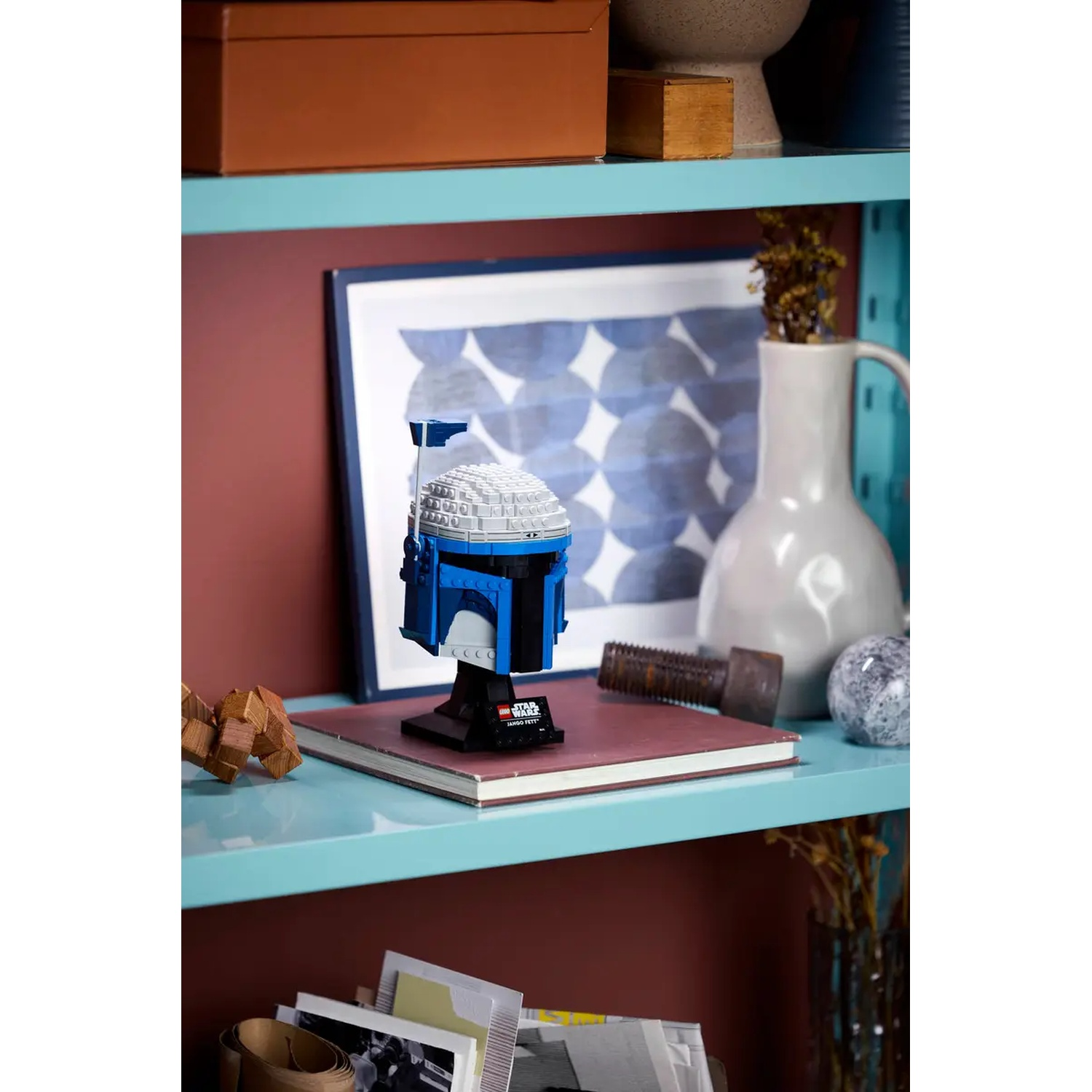 A Lego Star Wars helmet on a shelf. The helmet is blue and white, with a black stand. Other objects are on the shelf.