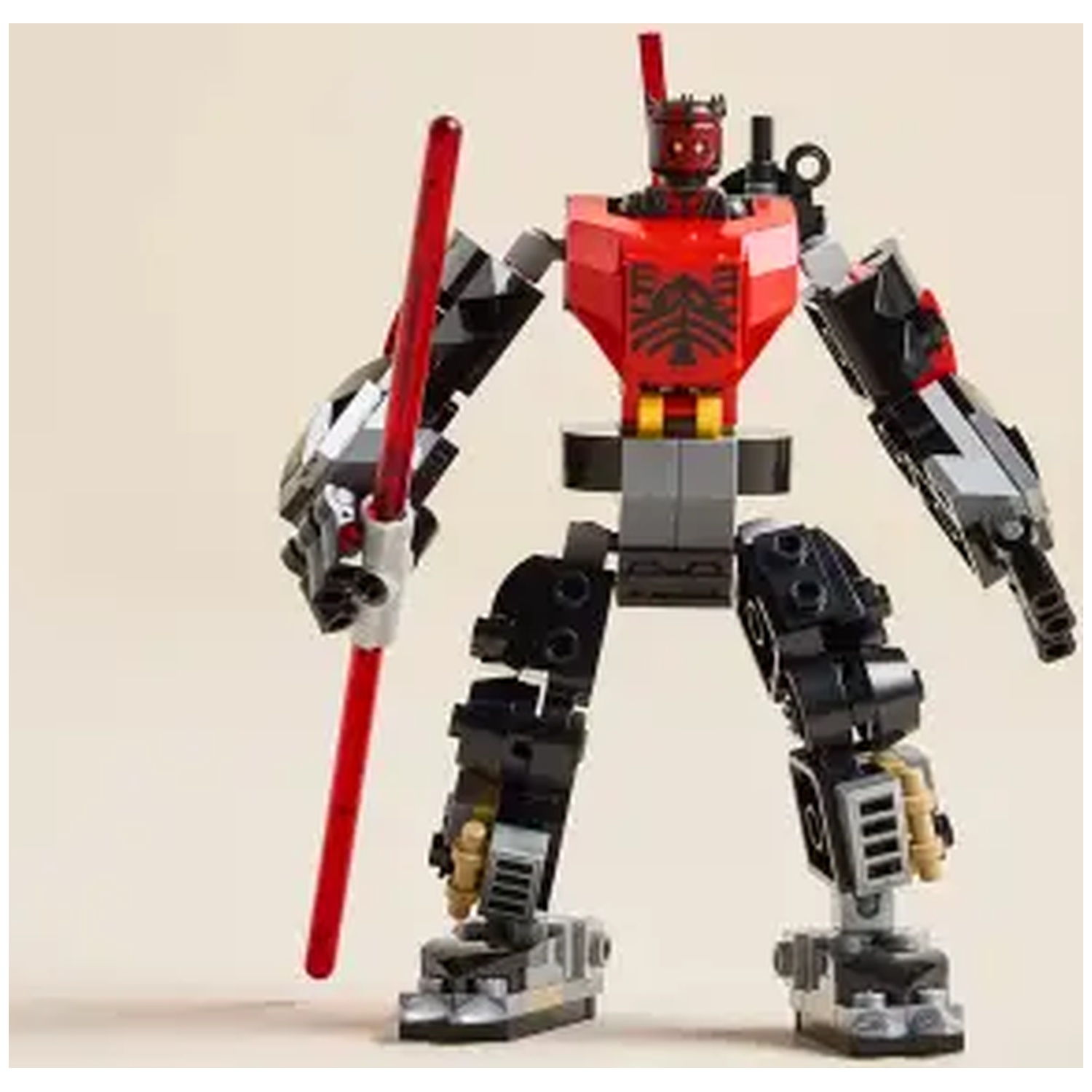 Een Lego robotfiguur met rood lichtzwaard, zwarte en rode romp, grijze en zwarte ledematen. Tegen een beige achtergrond.