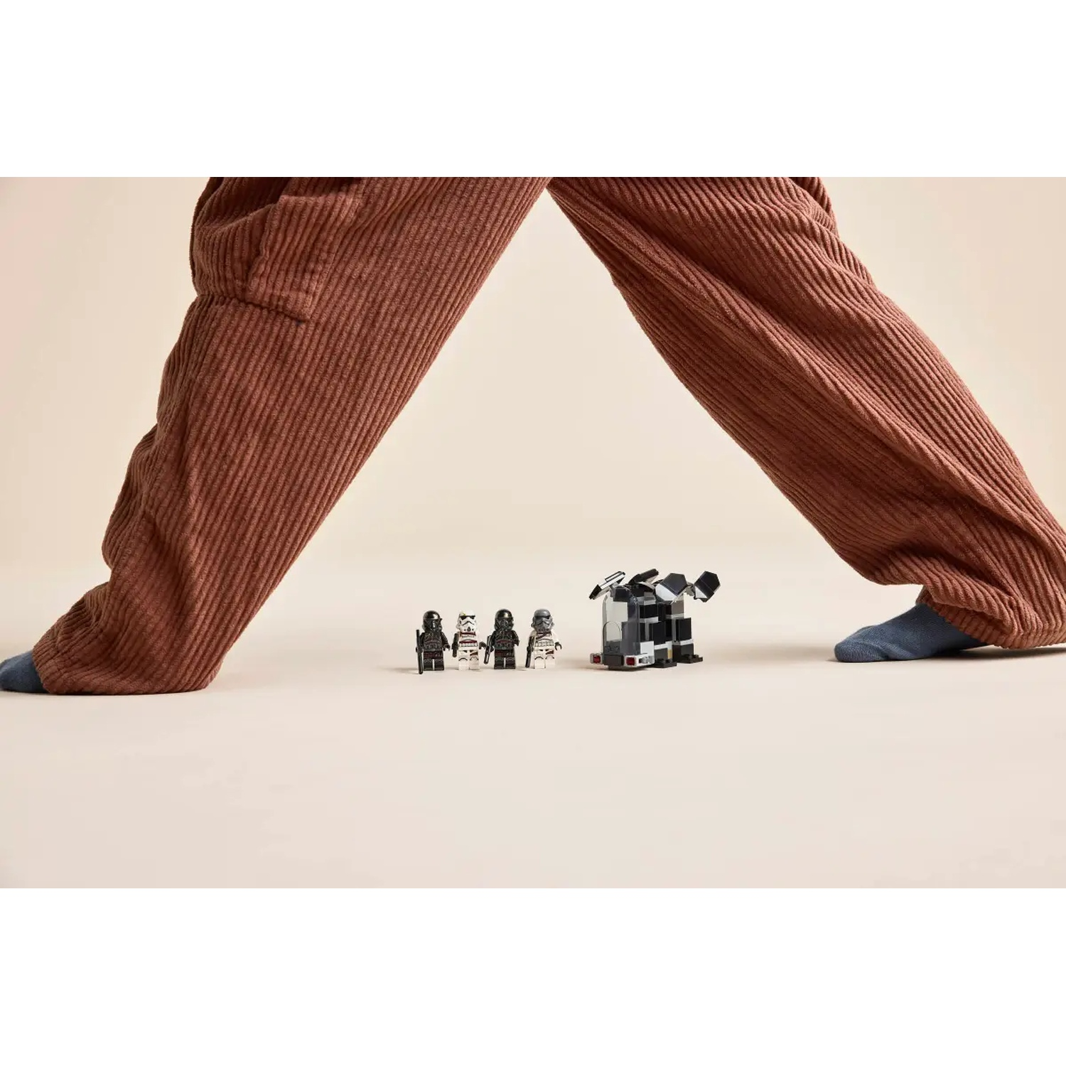 Person's legs in brown corduroy pants over small figurines and a Lego structure. Blue sock is visible.
