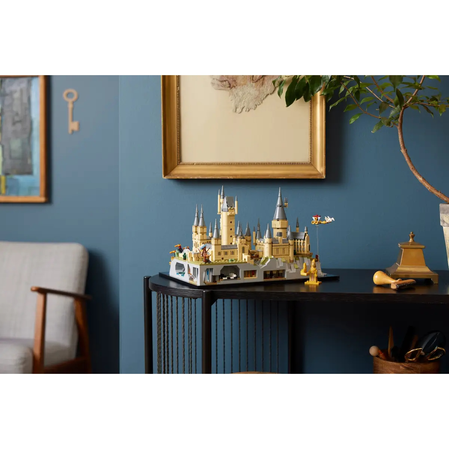Een Lego-kasteel staat op een zwarte tafel. Een sleutel en een lijst aan de blauwe muur. Een stoel links.