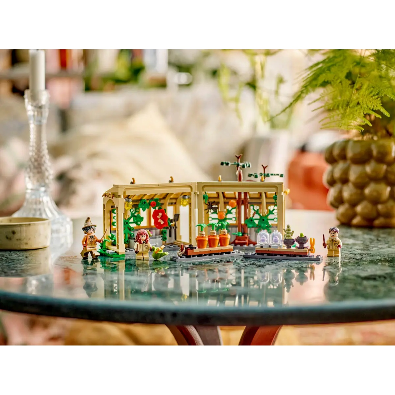 Lego set depicting a greenhouse scene with minifigures and plants. A candle and a vase are also visible.