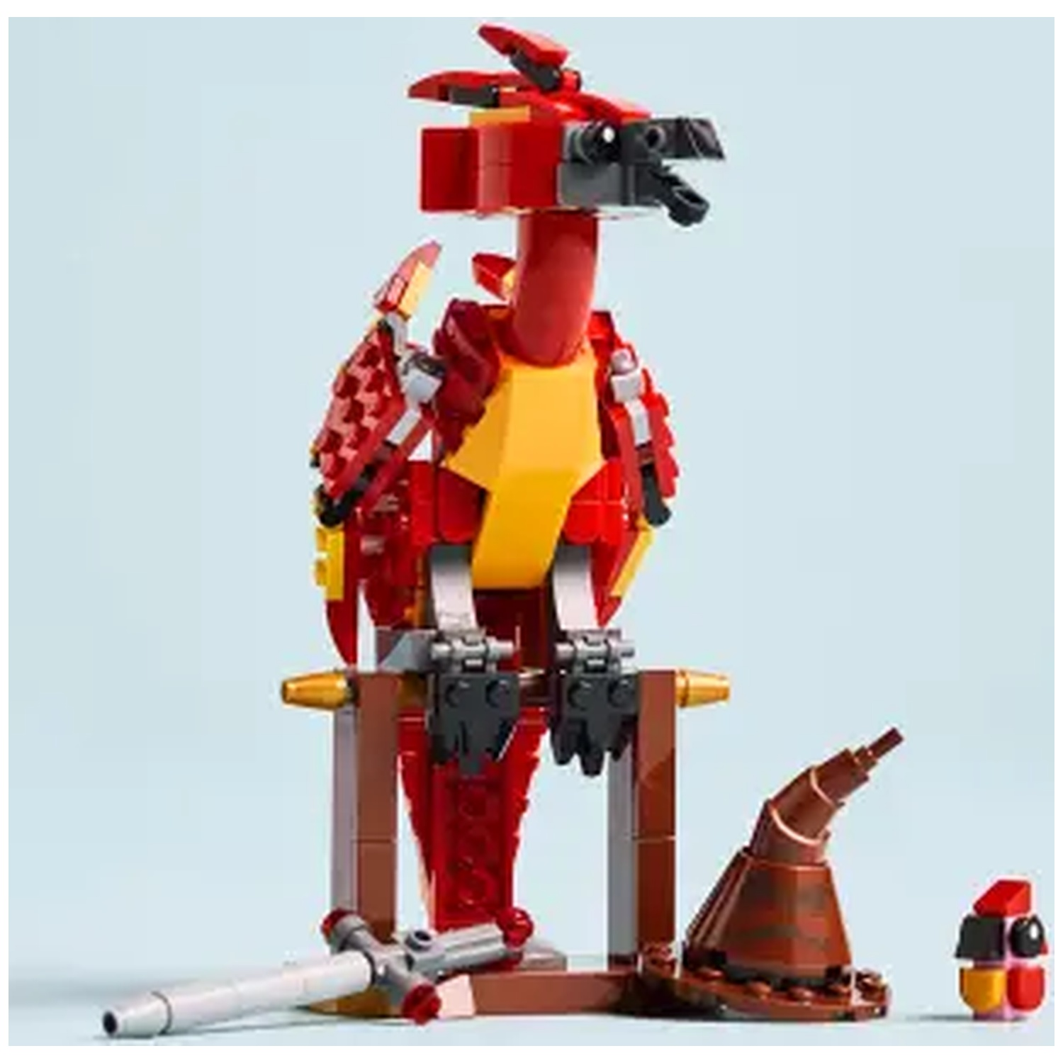 Een Lego Phoenix-speelgoed. Rode en gele vogel met een bruine standaard. Een toverstaf en een tovenaars hoed zijn ook aanwezig.