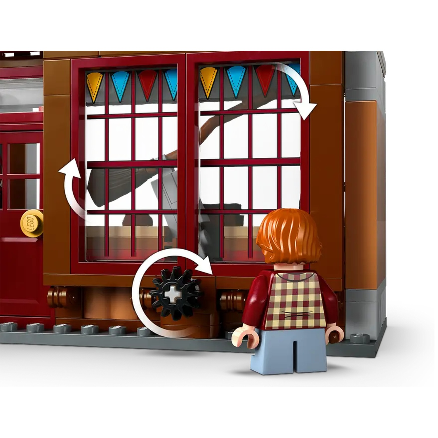 A Lego figure stands before a brown building with red accents, a large window, and colorful pennants. A gear is visible.
