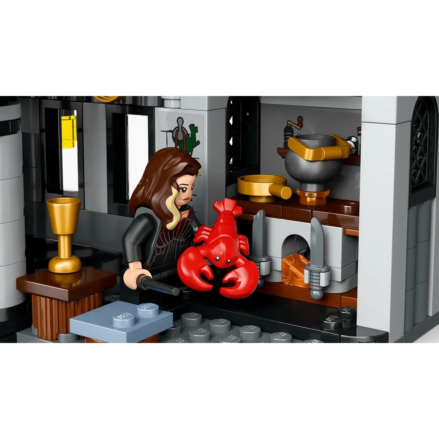 A Lego figure holds a red lobster. A gold goblet and a pot are visible. The scene is a kitchen, with grey walls and a table.