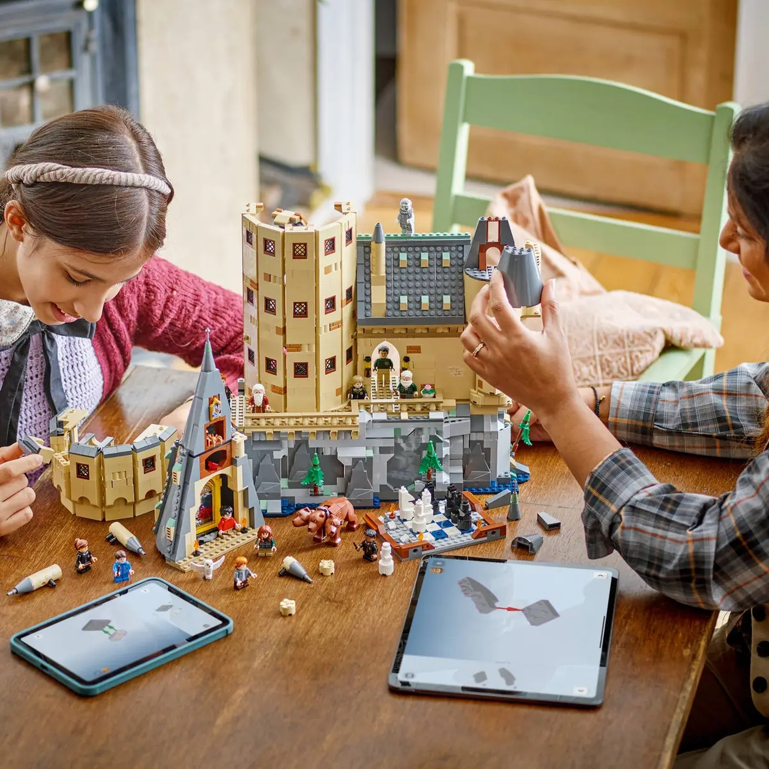 Twee mensen bouwen een Lego-kasteel. Een tablet toont instructies. Kasteel is beige, grijs en heeft kleine figuurtjes.