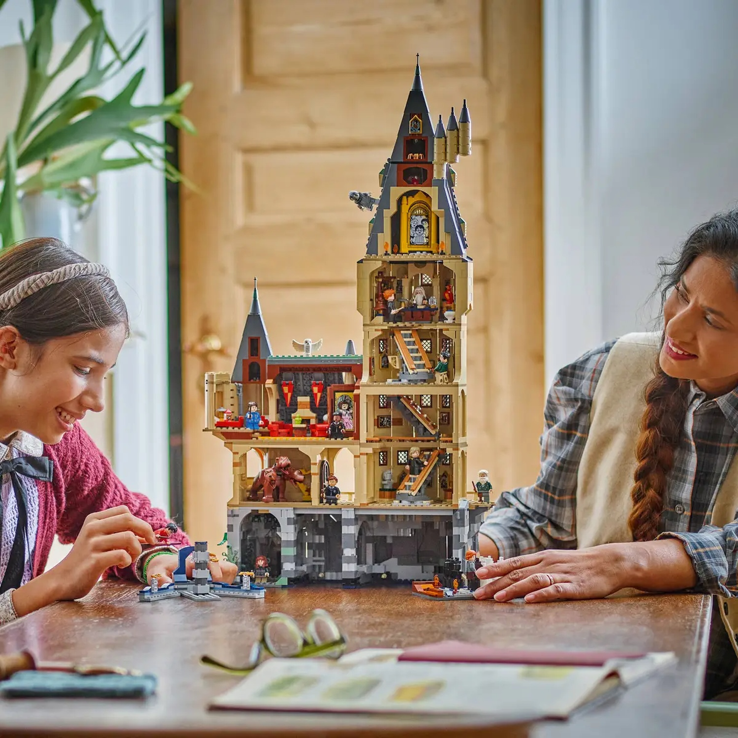 Twee vrouwen bouwen een Lego-kasteel en lachen naar het model. Het kasteel is meerlaags met veel figuren.