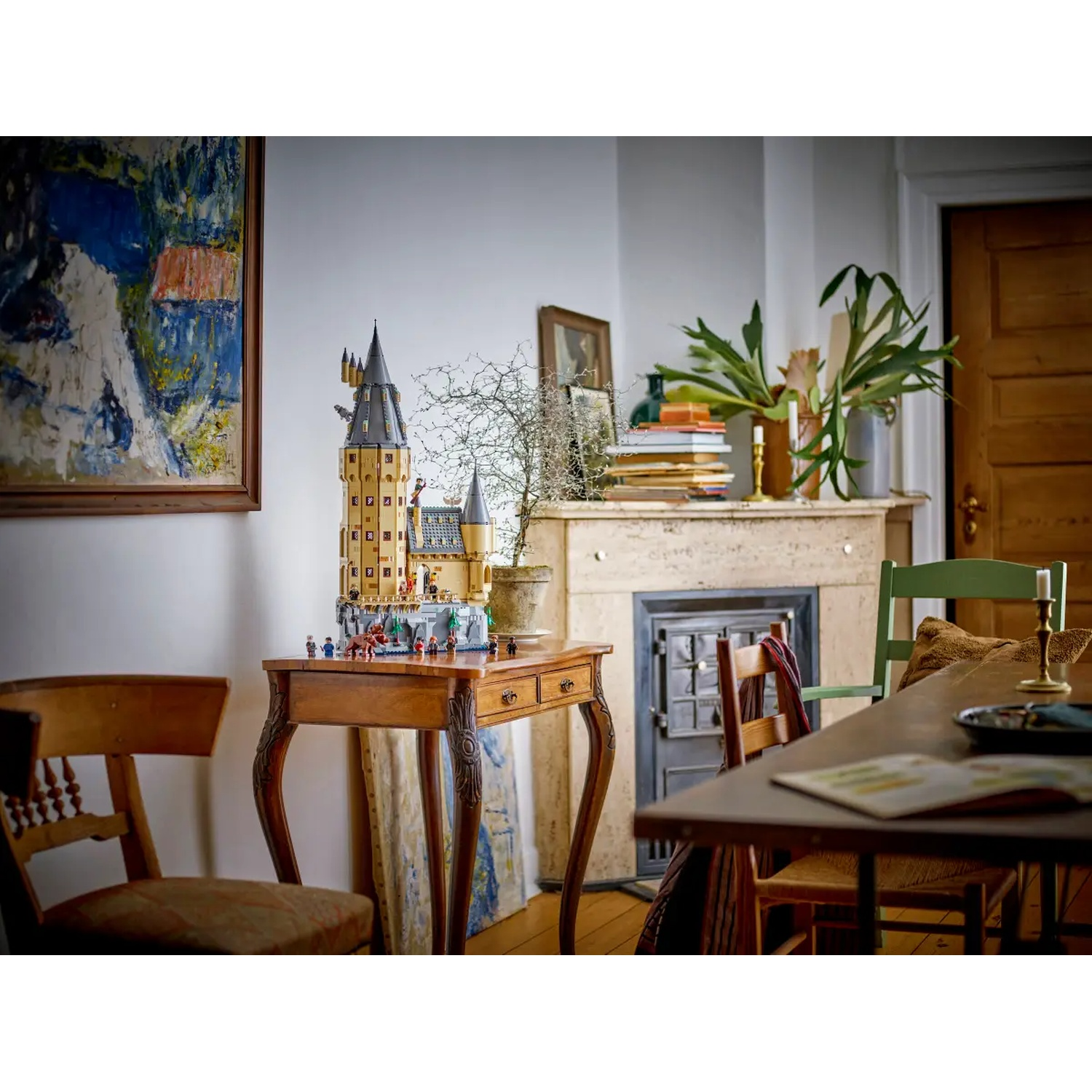 Een kamer met een Lego-kasteel op een tafel. Een schilderij, een open haard en stoelen zijn ook zichtbaar. Achterin een houten deur.