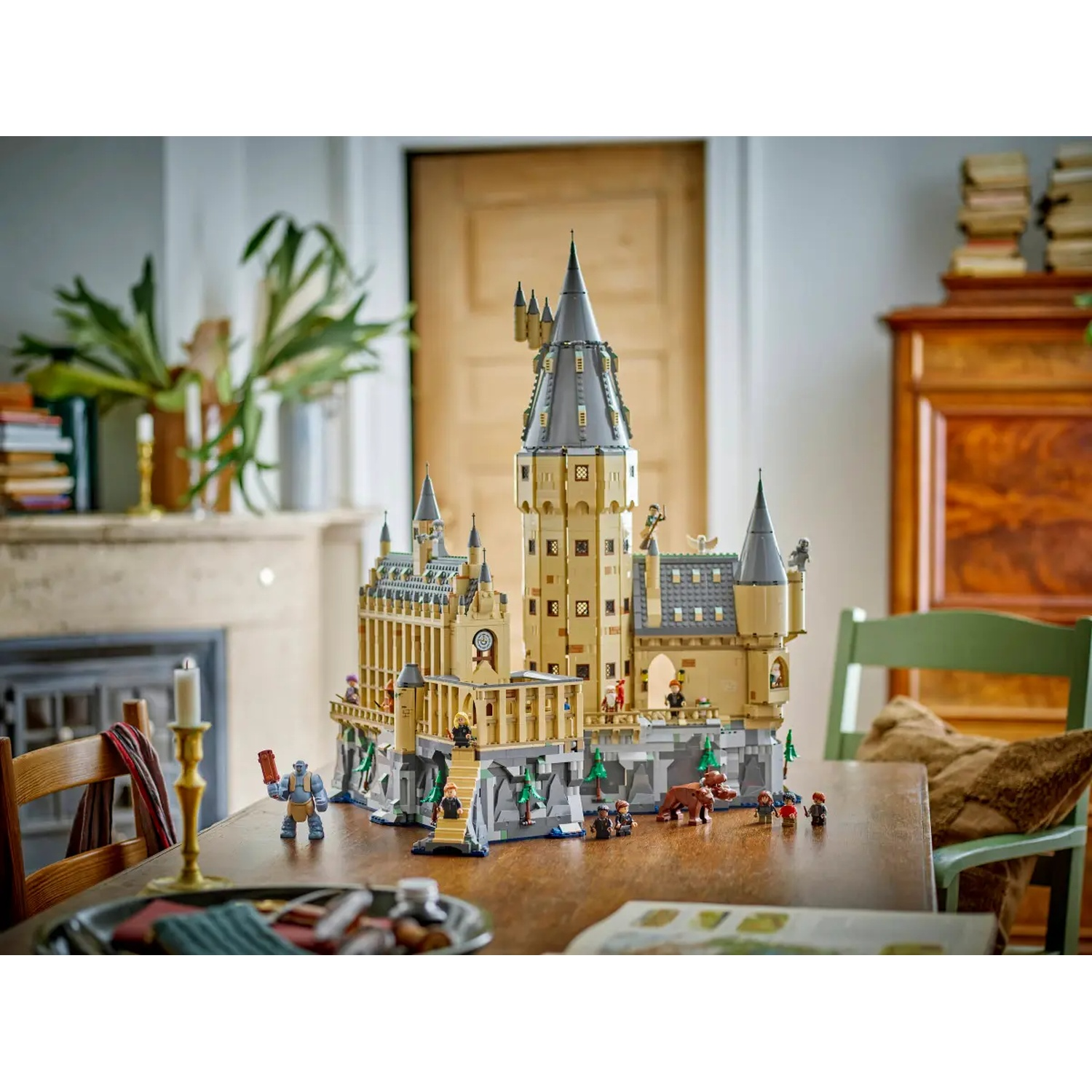 Een Lego kasteel staat op een houten tafel. Figuren zijn rondom het kasteel geplaatst. Een kaars en een groene stoel staan op de achtergrond.