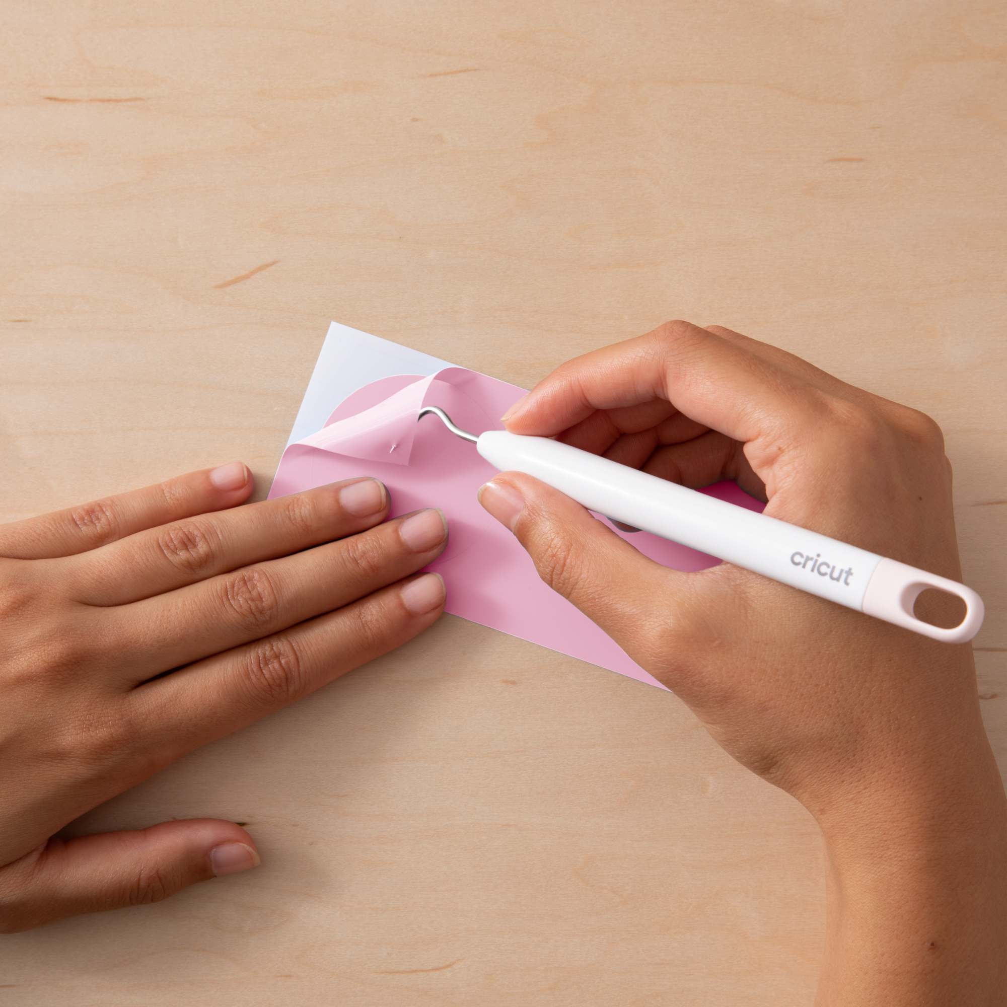 Hände, die einen rosa Aufkleber von einem weißen Blatt abziehen. Ein Cricut-Werkzeug wird verwendet.