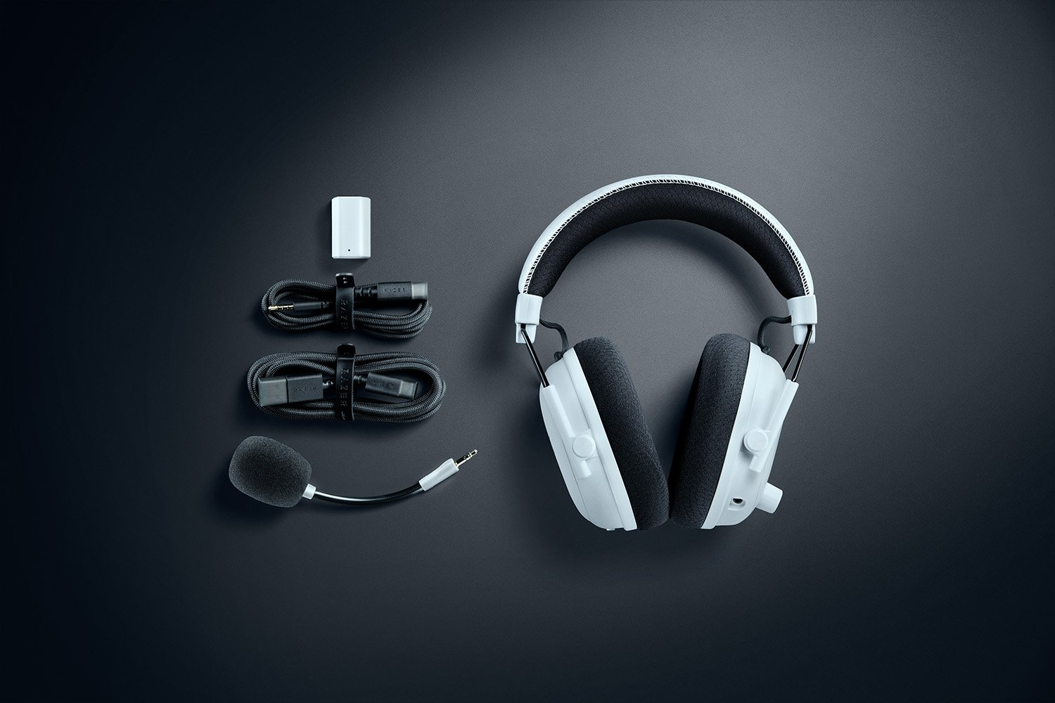 Kopfhörer, Mikrofon und Kabel auf dunkler Oberfläche. Das Headset ist weiß und schwarz, das Mikrofon ist schwarz.