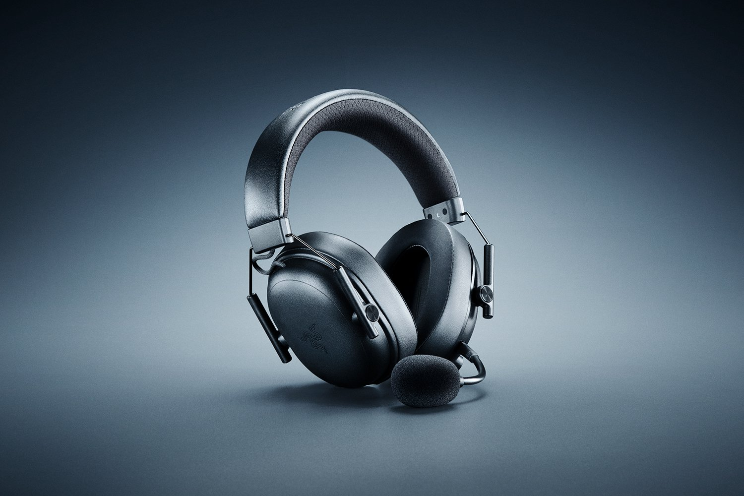 Cuffie da gaming nere con microfono, su una superficie grigia. Lo sfondo è un gradiente grigio e blu scuro.