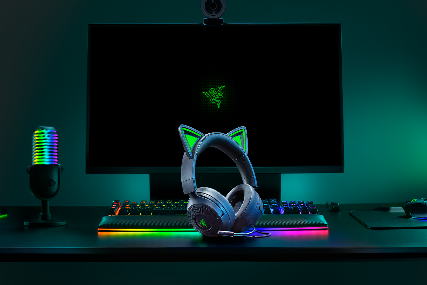 Configurazione di gioco con monitor, tastiera e cuffie con orecchie da gatto. Un microfono colorato a sinistra.