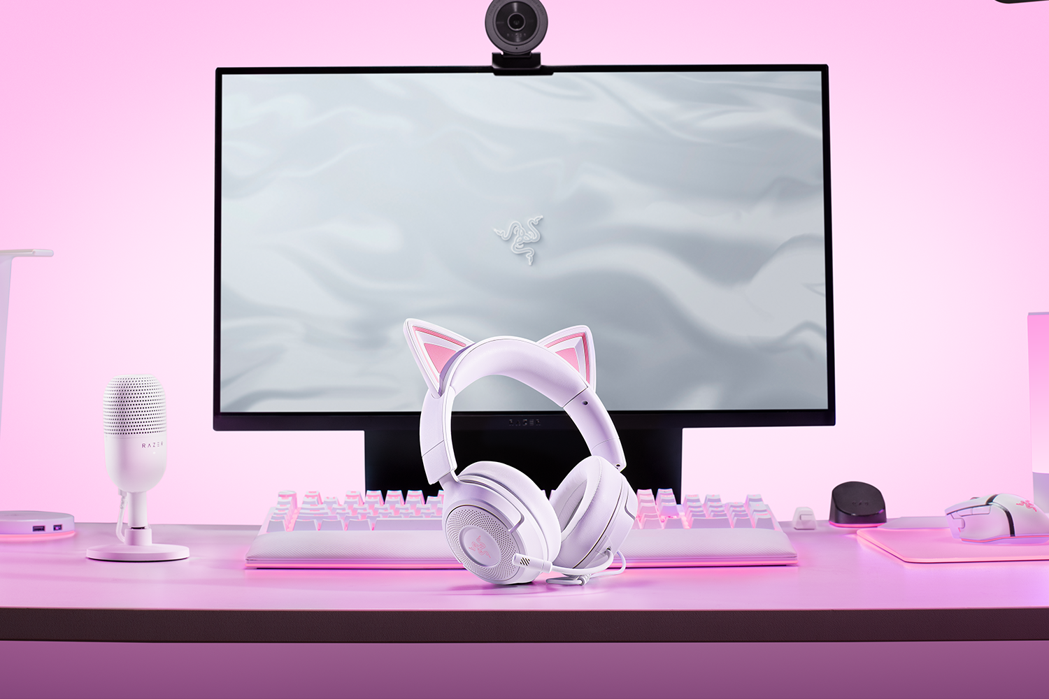Un'impostazione di gioco con una scrivania bianca. Include monitor, cuffie con orecchie da gatto, tastiera, microfono, mouse e webcam.