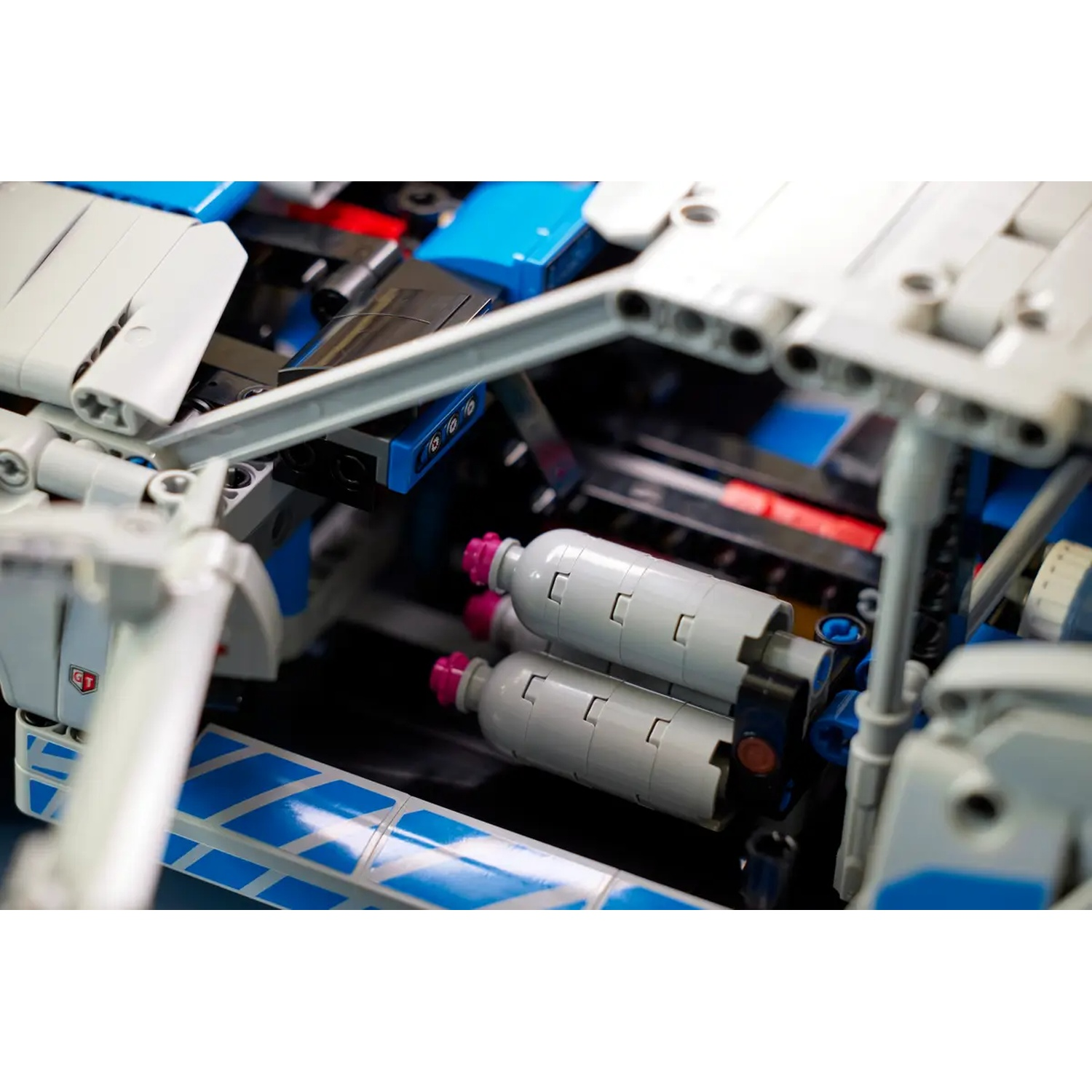 Close-up of a Lego Technic model. Gray and blue components are visible, including cylinders with pink accents and various structural elements.